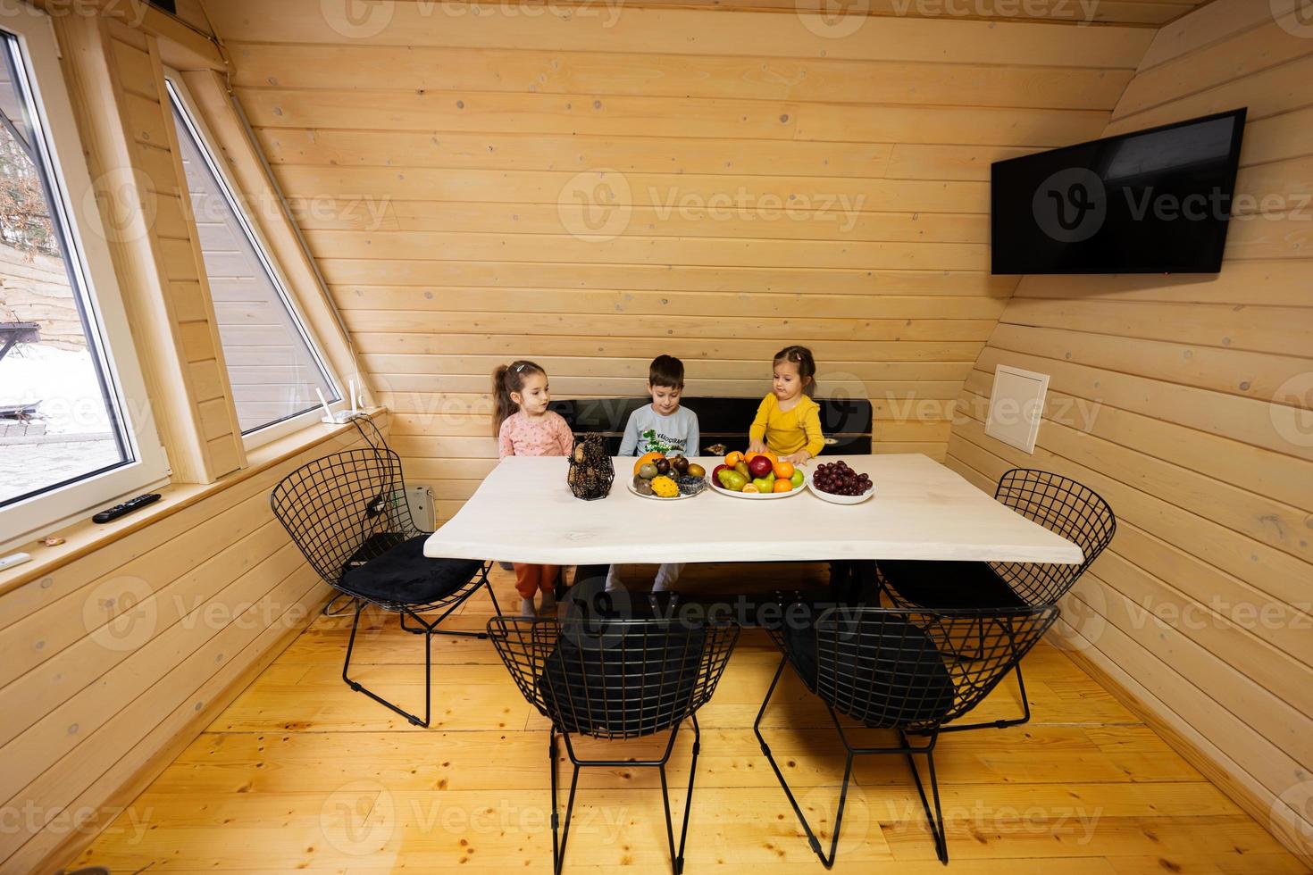 Trois les enfants manger des fruits dans en bois pays maison sur fin de semaine. photo