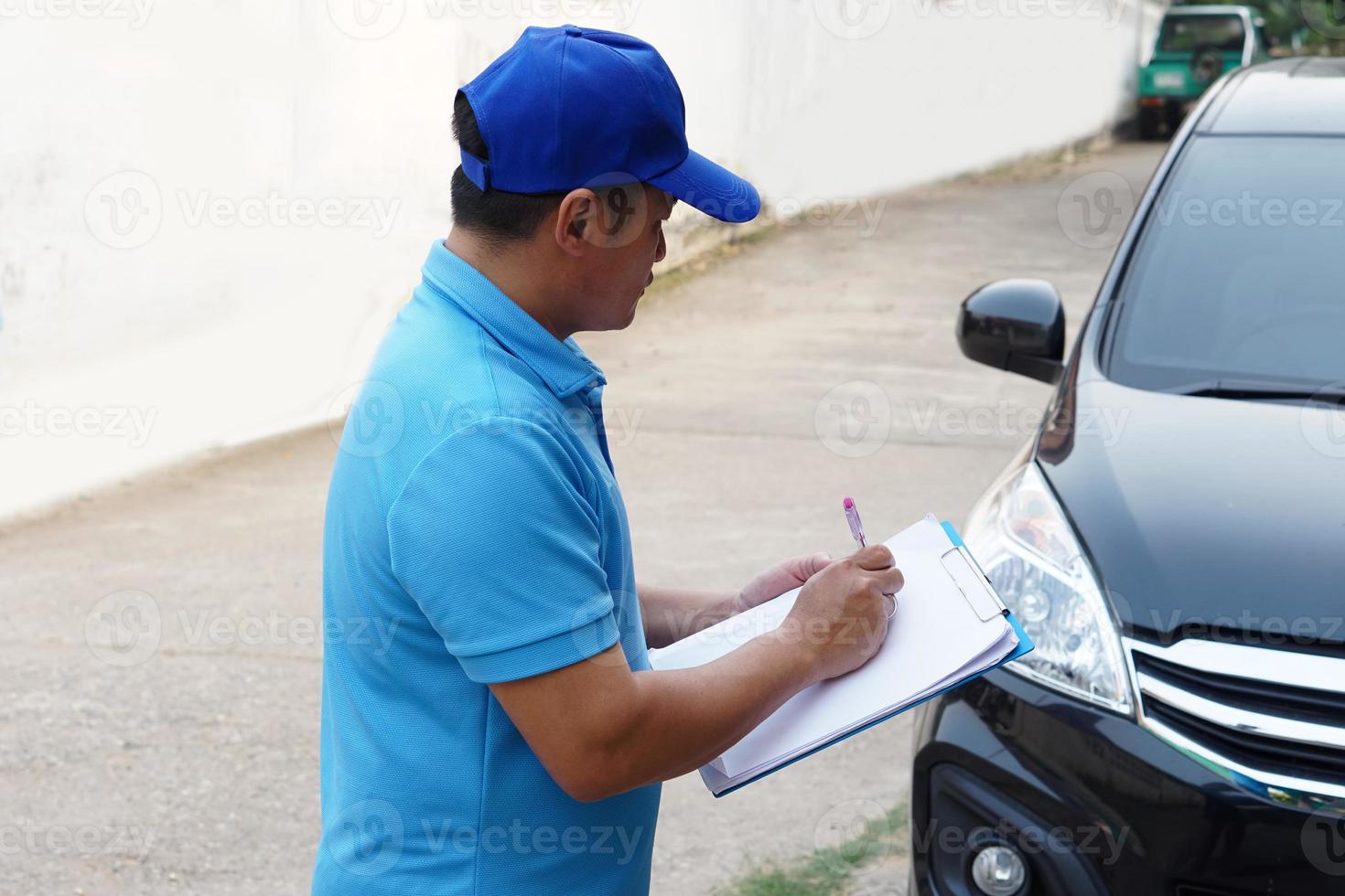 asiatique homme mécanicien porte bleu casquette et bleu chemise, détient papier bloc-notes, vérification et évaluer cassé voiture condition.concept, prétendre pour accident assurance. bord de la route assistance. Extérieur voiture service. photo