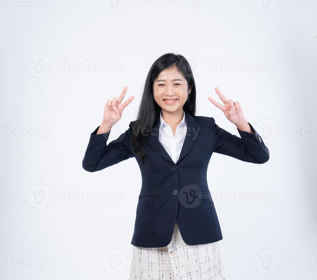 content Jeune brunette femme dans blanc chemise sur isolé Contexte. portrait de attrayant souriant fille à la recherche tout droit dans le caméra et montrant paix ou la victoire signe avec sa des doigts. deux des doigts. photo