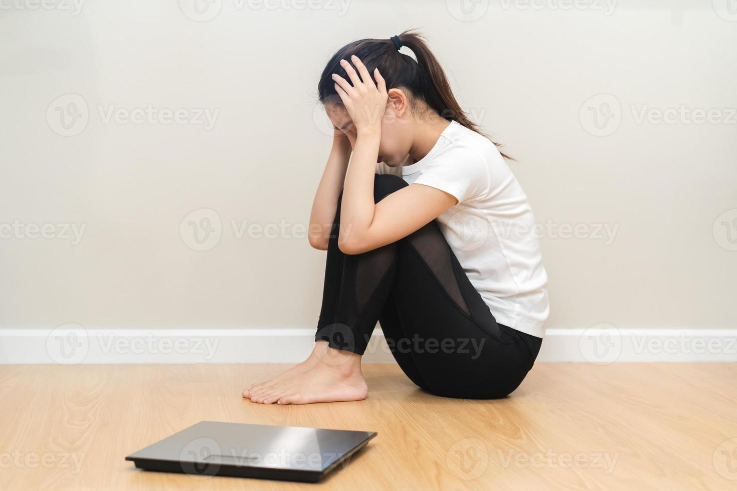 déprimé et stress, triste asiatique Jeune femme, fille couverture visage avec main, séance sur sol, pesée sur échelle dans de face de son. Gain perdre poids et en surpoids graisse. gens régime, mauvais pour la santé, malheureux concept photo