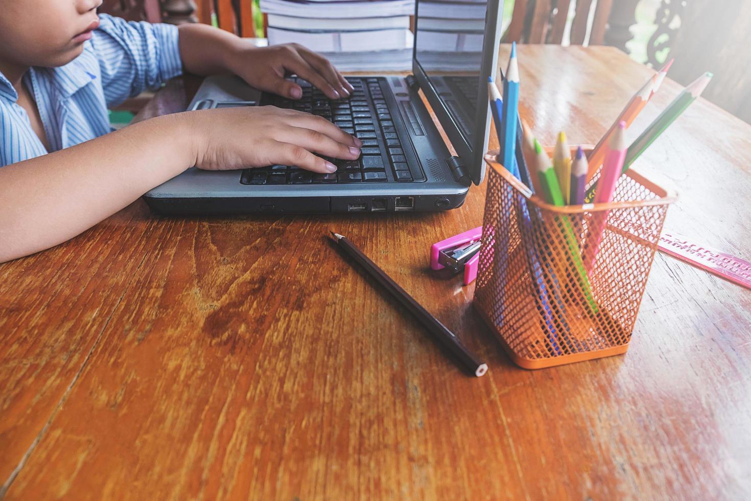 Garçon travaillant sur un ordinateur portable à côté d'une tasse de crayons sur un bureau en bois photo