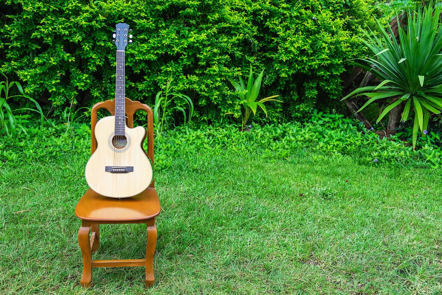 Guitare acoustique sur une chaise en bois dans une cour d'arbustes photo