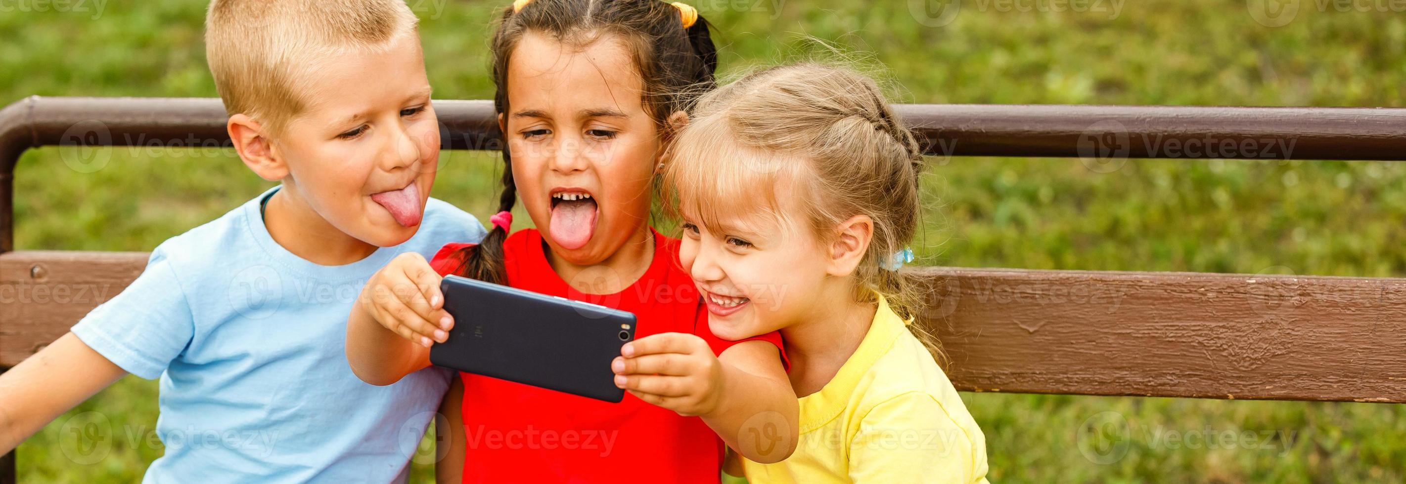 groupe de les enfants séance sur banc dans centre commercial prise selfie photo