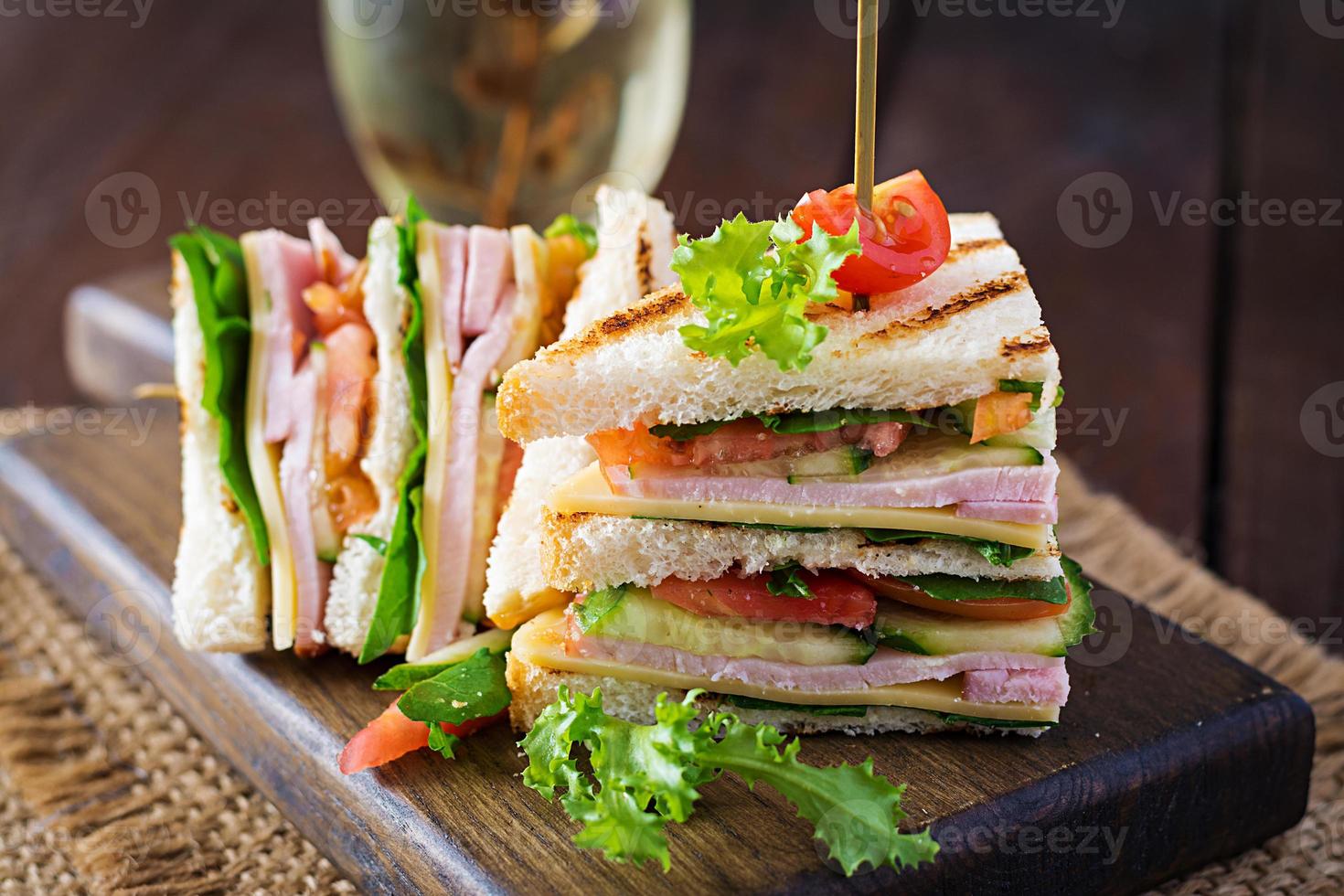 club sandwich avec jambon, tomate, concombre, fromage, et Roquette sur en bois Contexte. photo