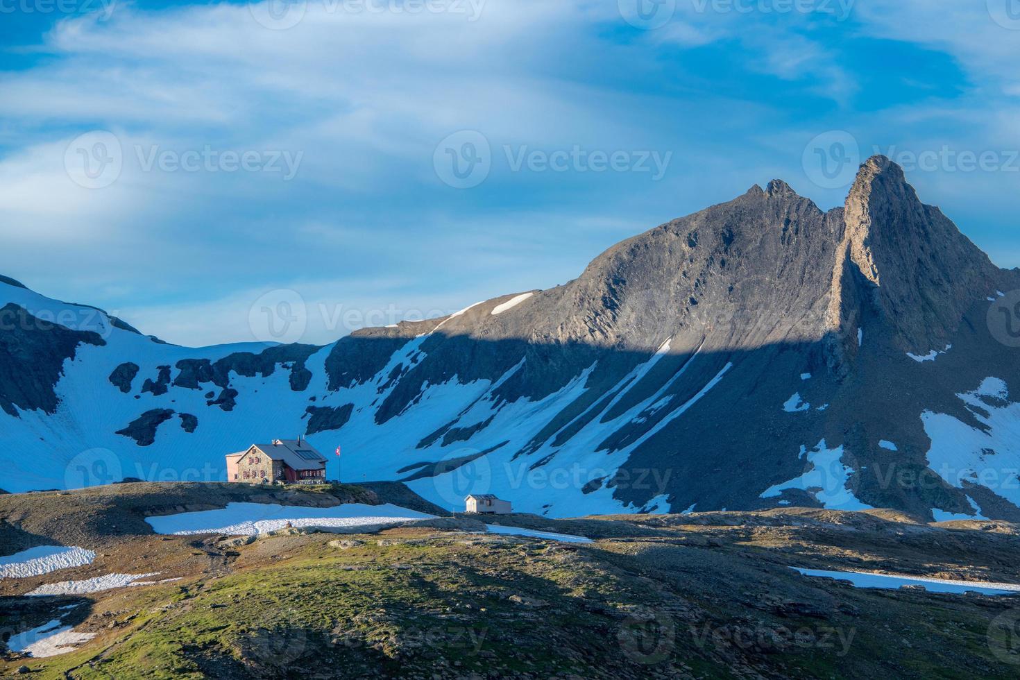 une Suisse Montagne auberge des stands en haut dans le montagnes en dessous de une légèrement nuageux ciel photo