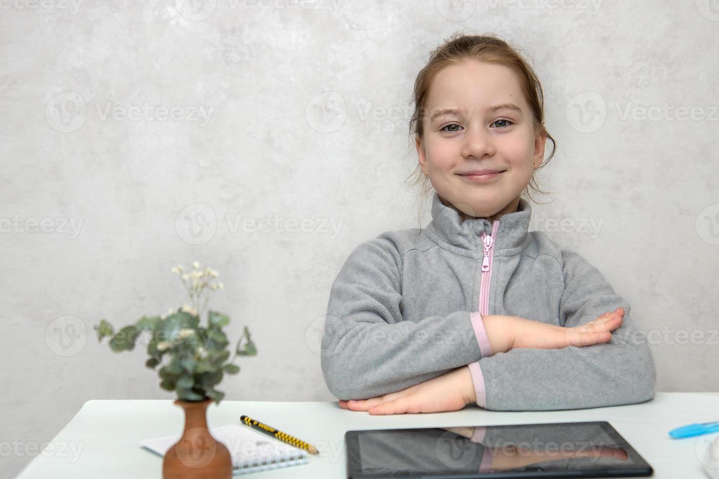 peu mignonne fille étudiant avec une sourire est assis à une bureau avec sa mains étreint prêt pour Des classes, retour à école photo