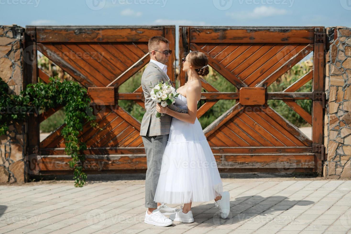 Jeune couple la mariée dans une blanc court robe et jeune marié dans une gris costume près le en bois porte photo