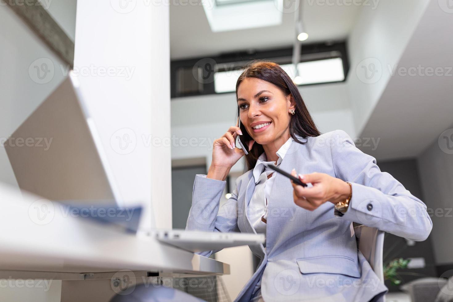 femme travail sur portable à Bureau tandis que parlant sur téléphone, tandis que dans quarantaine isolement pendant le covid-19 santé crise. portrait de une magnifique affaires femme souriant et à la recherche à portable écran photo