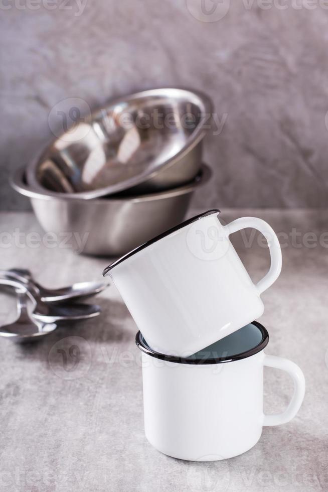 deux blanc vide métal des tasses et métal boules et cuillères sur une gris verticale Contexte photo