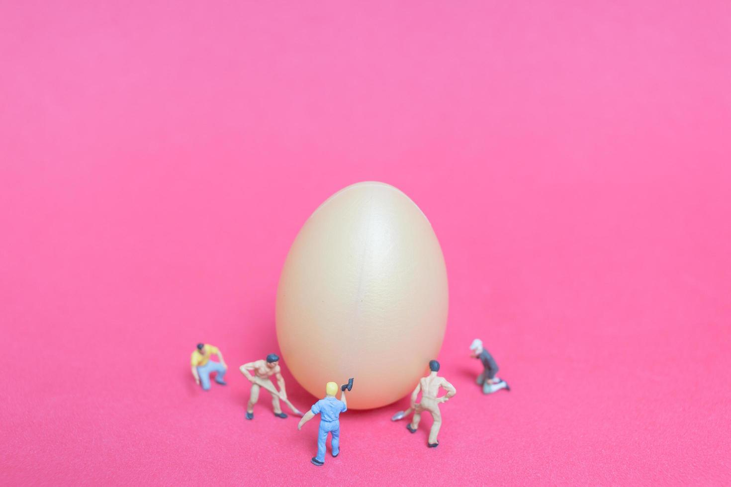 Personnes miniatures travaillant sur les oeufs de Pâques pour le jour de Pâques sur fond rose photo