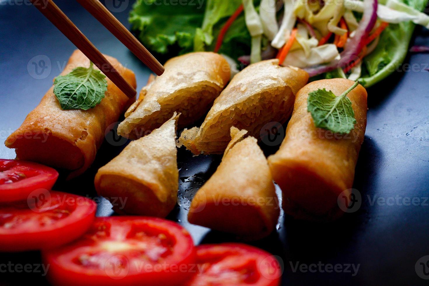 frit printemps Rouleaux avec des légumes et tomates mis dans une noir assiette sur une noir en bois table et plongement sauce. photo