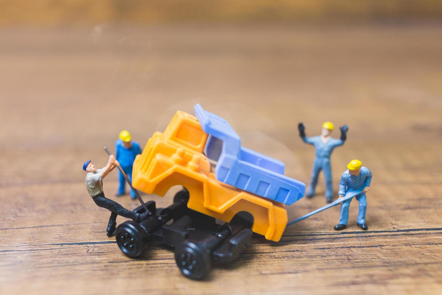 Travailleurs miniatures réparant une roue d'un camion sur un fond de bois photo