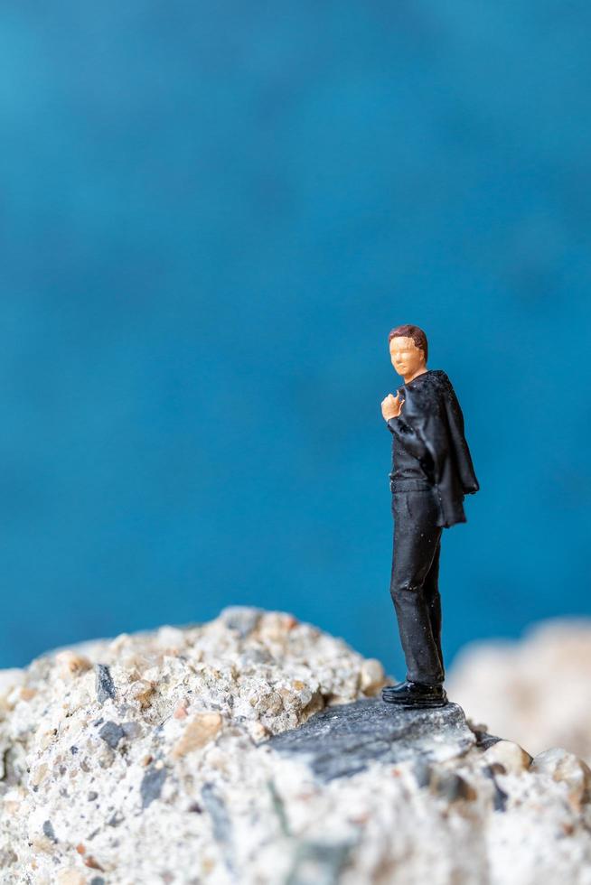 homme d & # 39; affaires miniature debout sur un rocher avec un fond bleu photo