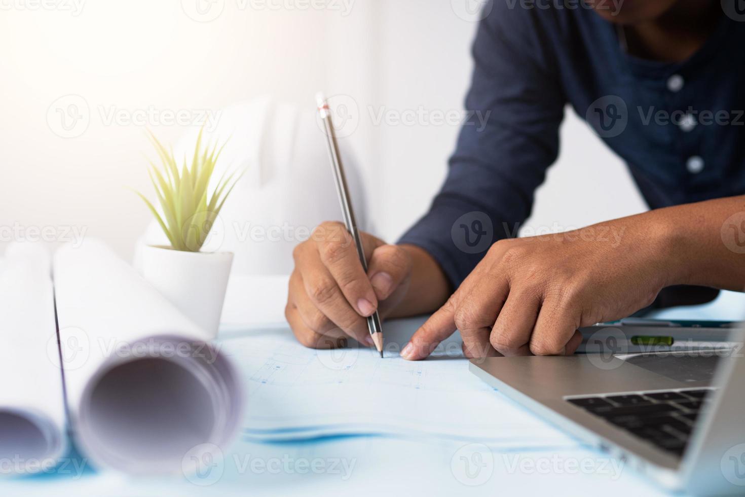 architecte travaillant sur un plan à côté de l'ordinateur portable et du papier en rouleau photo