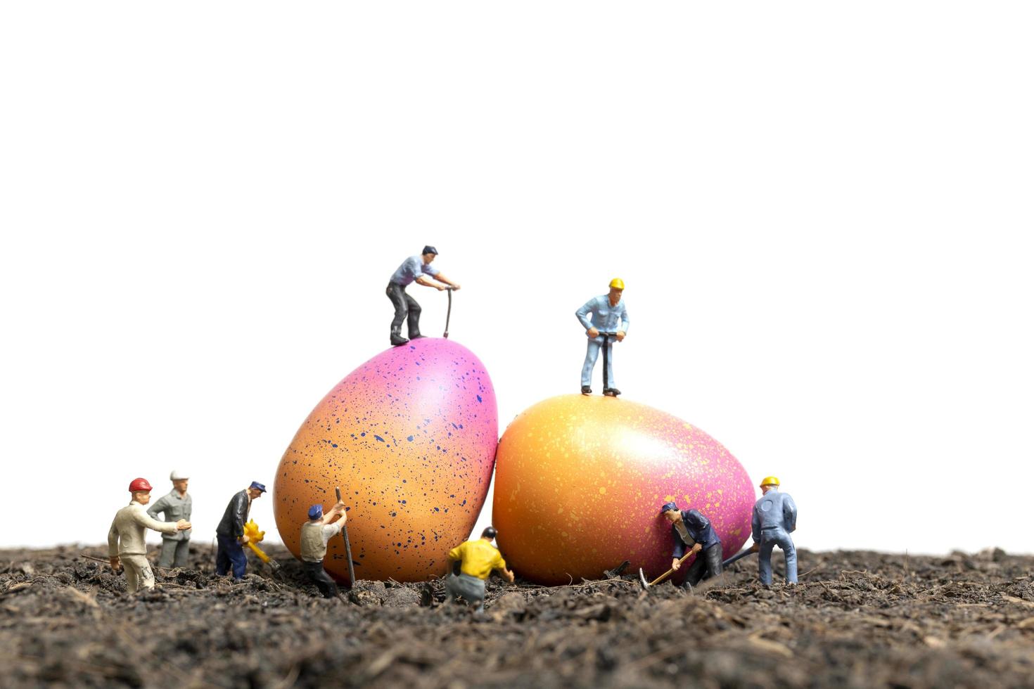 Les gens miniatures travaillant sur les oeufs de Pâques pour le jour de Pâques avec un fond blanc photo