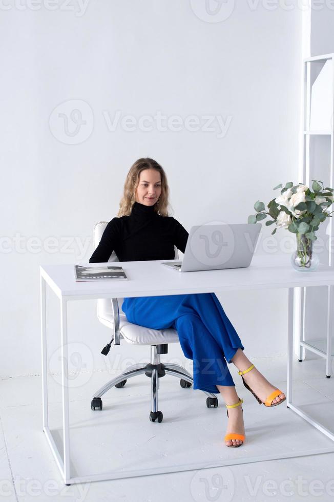 le fille travaux dans une blanc Bureau avec une portable et fleurs sur le table photo