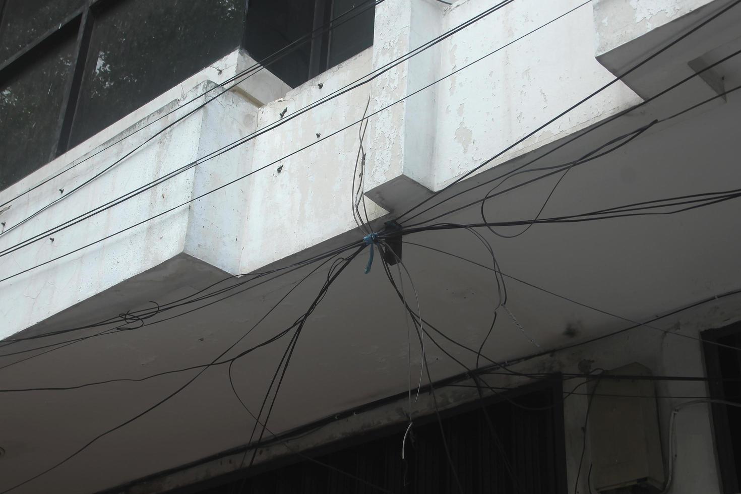 désordonné lié en haut noir électrique câble fils à l'extérieur sur le toit isolé sur rouillé vieux vieilli blanc des murs. photo