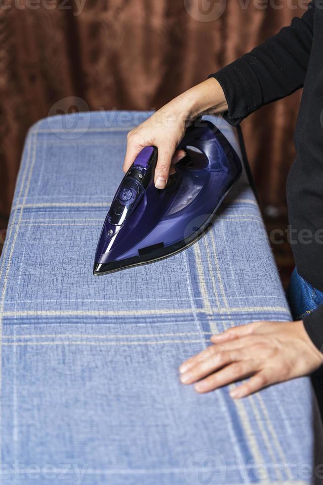 aux femmes mains tenir un le fer et le fer vêtements sur un repassage planche à maison, mode de vie photo