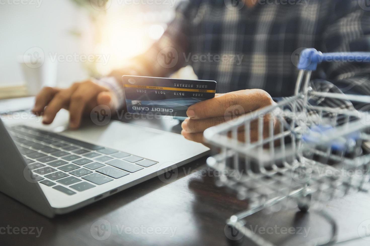 homme tenant une carte de crédit et travaillant sur un ordinateur portable à côté de panier miniature photo