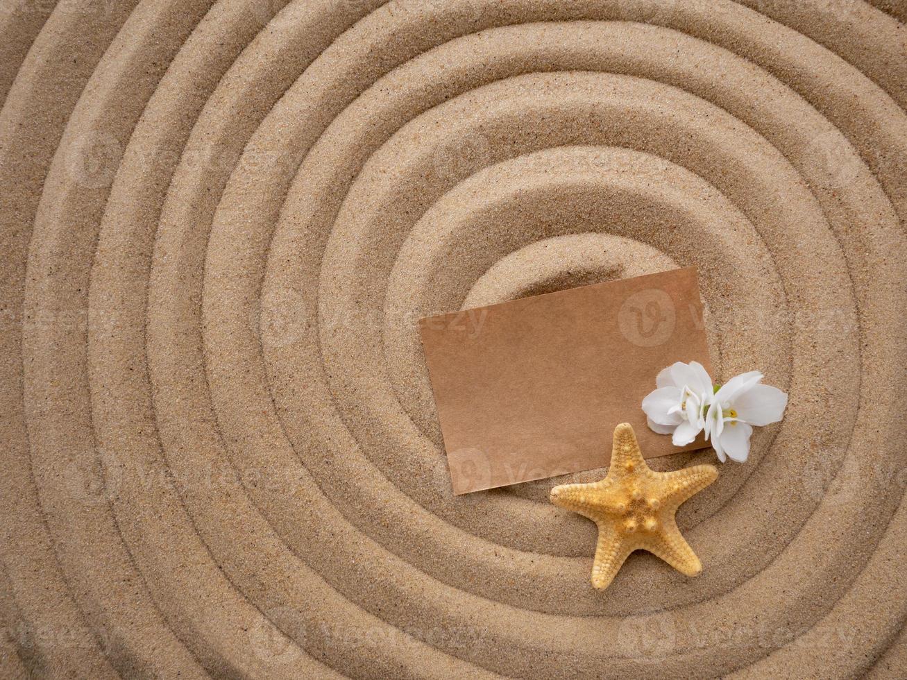 lettre dans le sable. artisanat papier avec une blanc fleur et une étoile de mer sur le sable dans le forme de une spirale. plage vacances, Zen photo