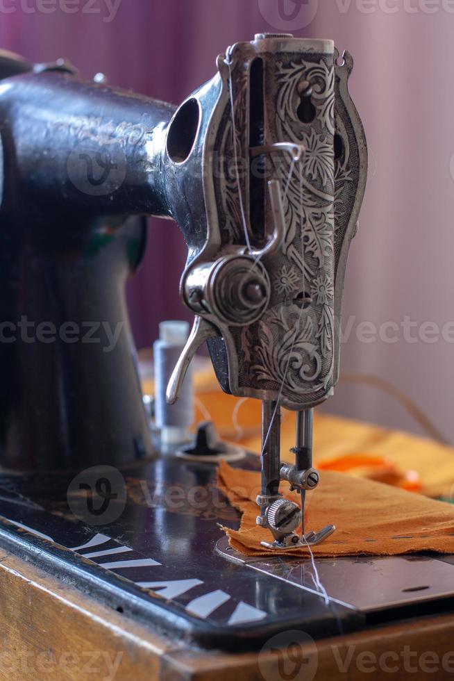vieux rétro couture machine et Orange en tissu prêt pour couture. le presseur pied est abaissé. peu profond profondeur de champ. concentrer sur le presseur pied. vertical. photo