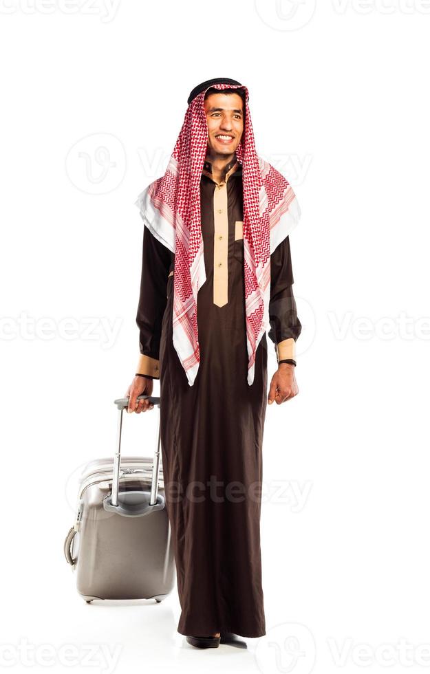 Jeune souriant arabe avec une valise isolé sur blanc photo