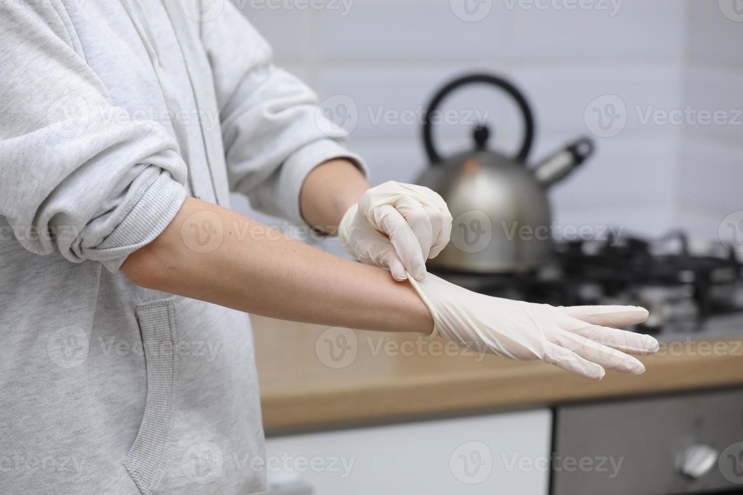 Jeune femme en mettant sur protecteur gants sur mains tandis que travail de Accueil ou à le Bureau travail par le table portable dans journée empêcher virus propager pendant épidémie dans quarantaine. sélectif concentrer photo