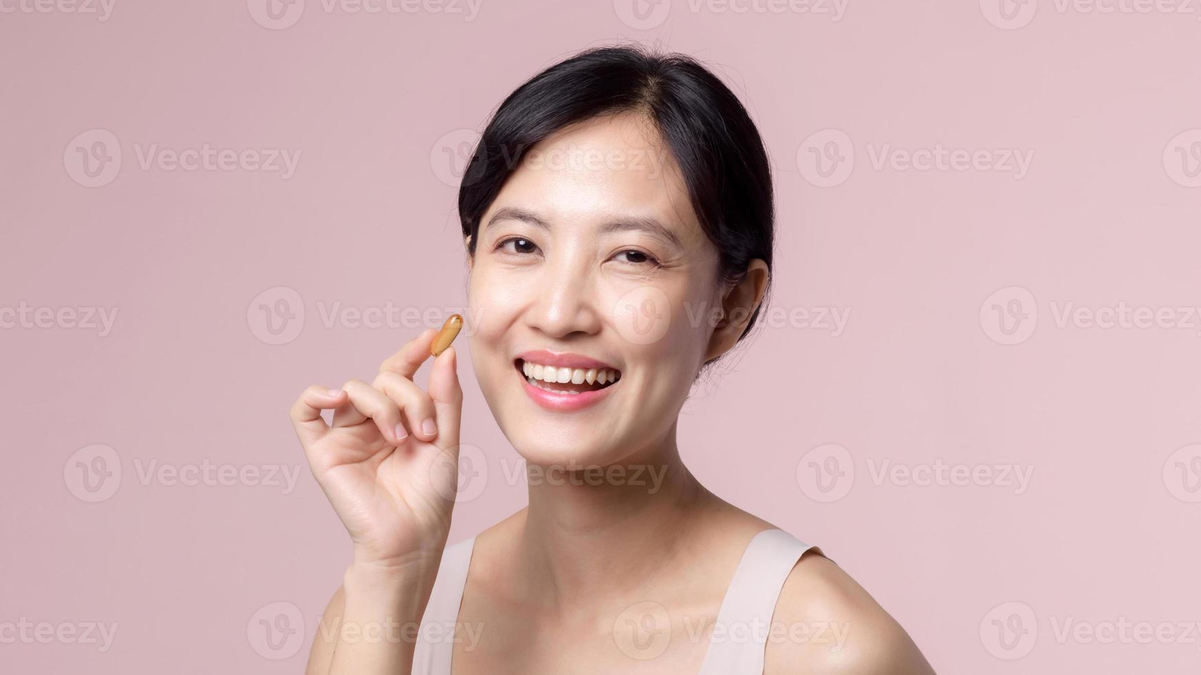 portrait Jeune asiatique femme content sourire visage avec vitamine nourriture pilule. jolie mignonne fille femelle la personne en portant santé capsule supplément peau se soucier isolé sur rose Contexte. des médicaments concept. photo