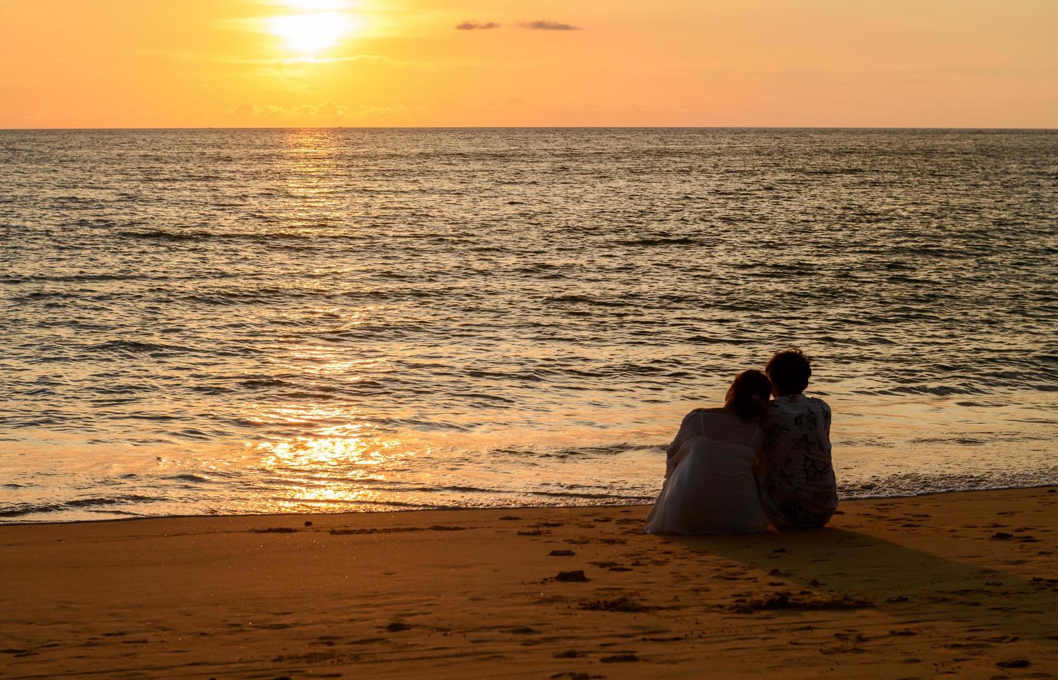 une couple est assis sur le plage en train de regarder le le coucher du soleil à Khao lak photo