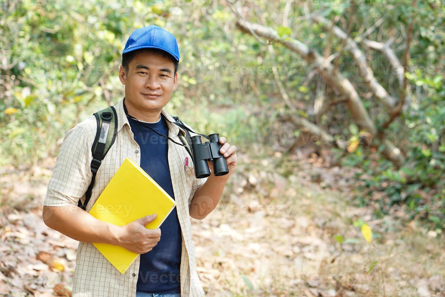 asiatique homme explorateur porte bleu casquette, détient binoculaire dans forêt à enquête botanique les plantes et créatures faune. concept, la nature exploration. écologie et environnement. photo