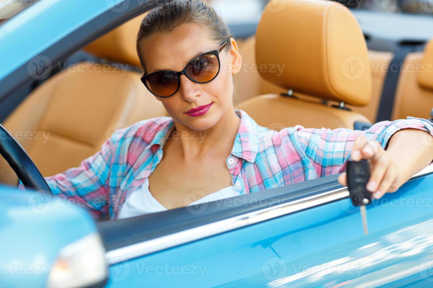 Jeune jolie femme dans des lunettes de soleil séance dans une convertible voiture avec le clés dans main photo