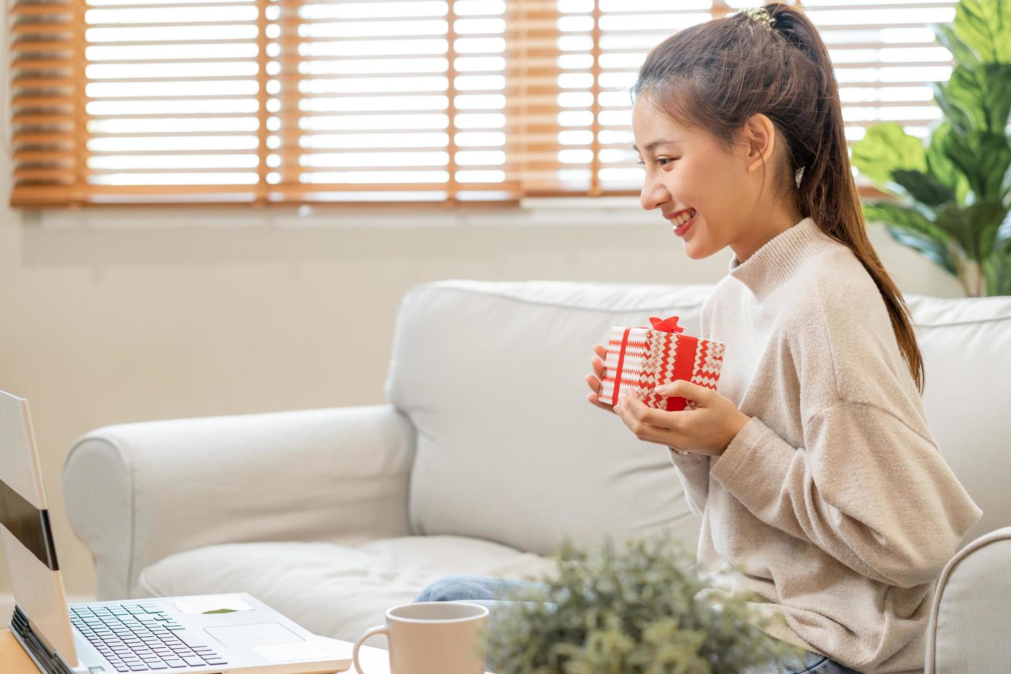 célébrer sur journée de aimer, Nouveau année journée saison, jolie asiatique Jeune femme, fille en utilisant portable ordinateur, salutation sur vidéo appel pendant social distance, en portant cadeau boîte, content à avoir présent sur Valentin. photo