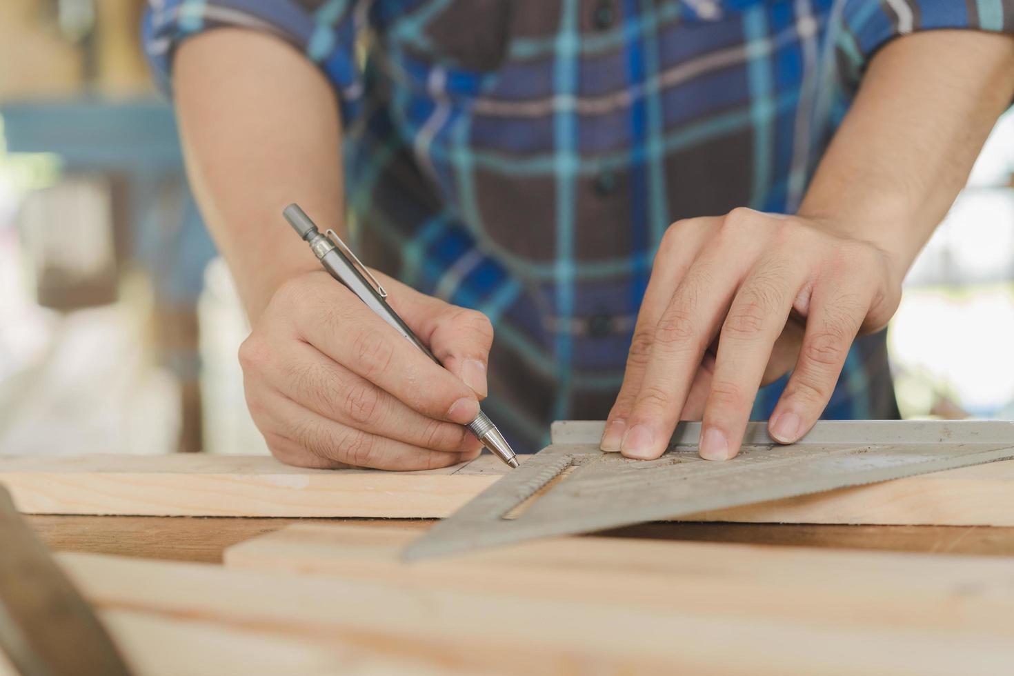 charpenterie professionnel, main de asiatique Jeune homme, Masculin Charpentier utilisation règle mesure, outil sur planche bois dans petit magasin. boiseries, meubles fabrication, construction industrie. propriétaire petit affaires personnes. photo