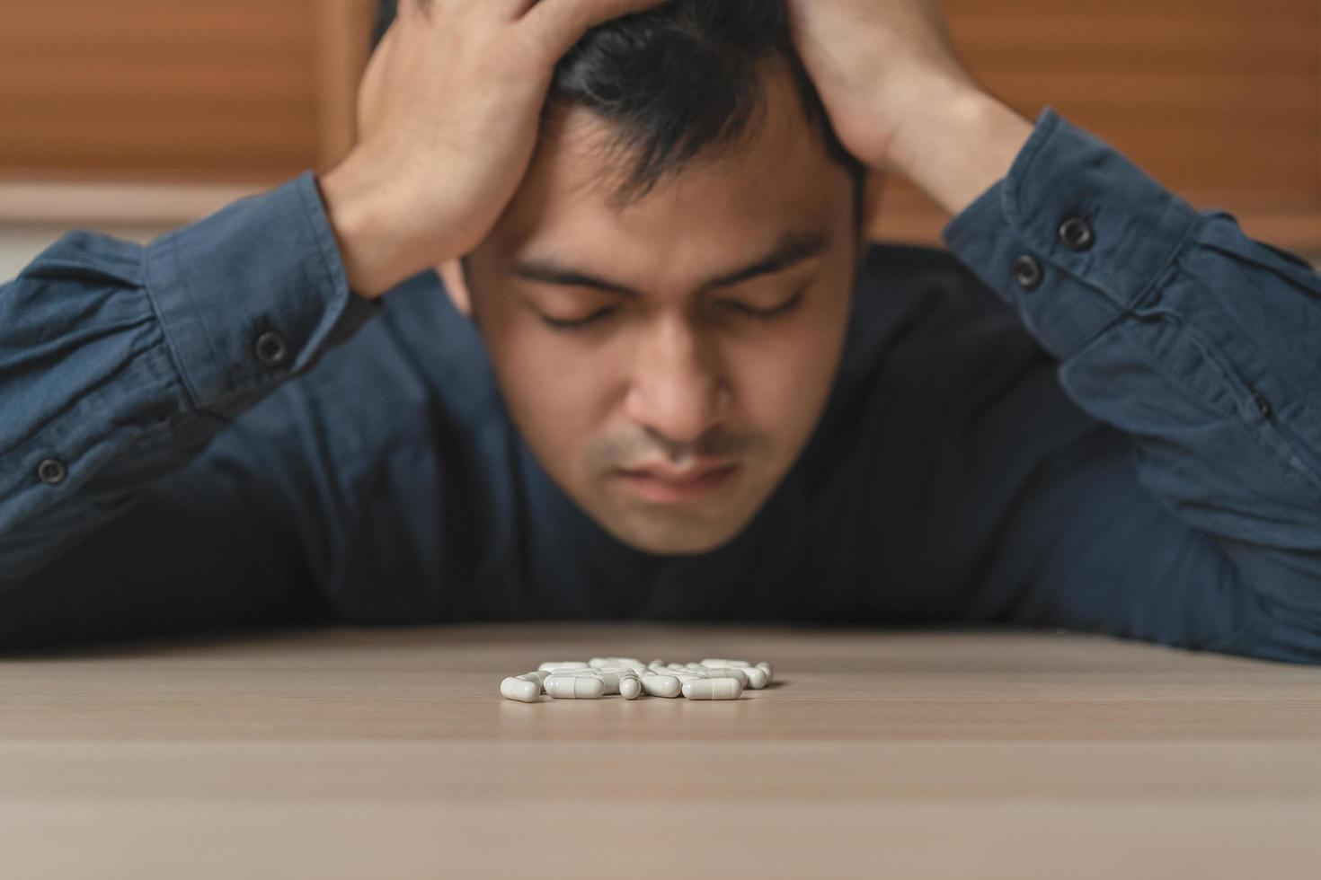 stressé, triste asiatique Jeune homme, Masculin en portant médecine, mensonge sur tableau. proche en haut main de abuser de surdosage pilules et toxicomane. malade douleur de santé traitement, malheureux personnes. suicide déprimé ou désespoir. photo