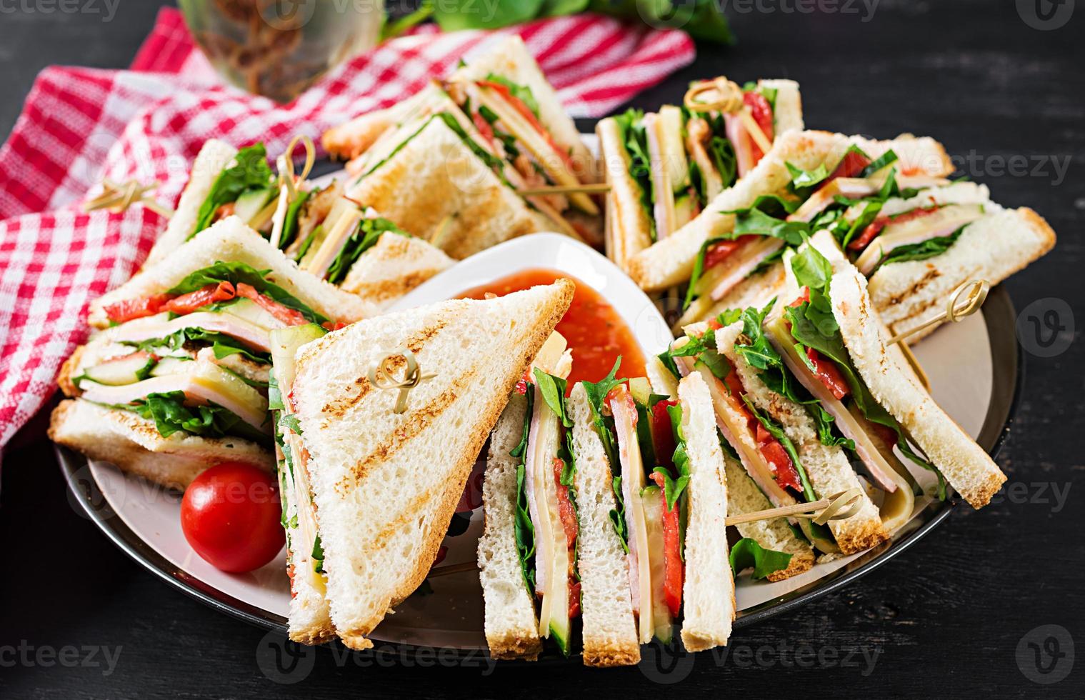 club sandwich avec jambon, tomate, concombre, fromage, et Roquette sur foncé Contexte. photo