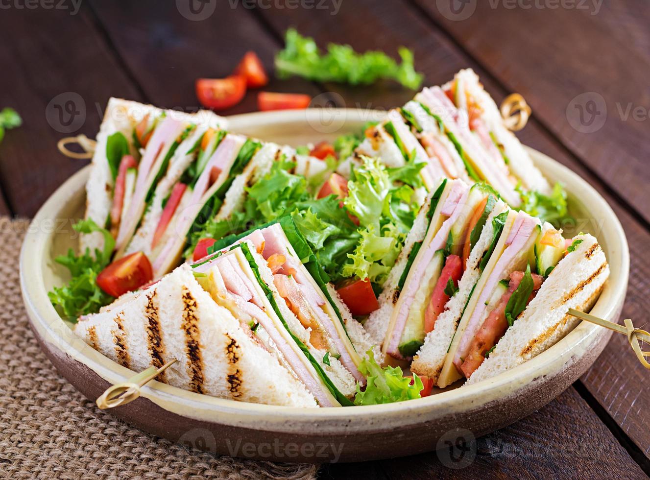 club sandwich avec jambon, tomate, concombre, fromage, et Roquette sur en bois Contexte. photo