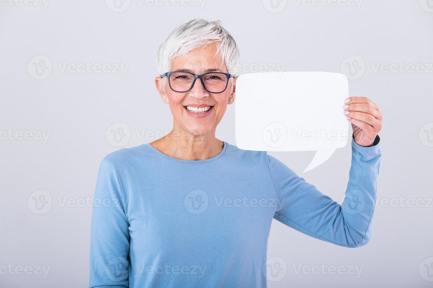 magnifique mature femme avec des lunettes en portant discours bulle avec sa mains et souriant à le caméra , isolé plus de gris Contexte photo