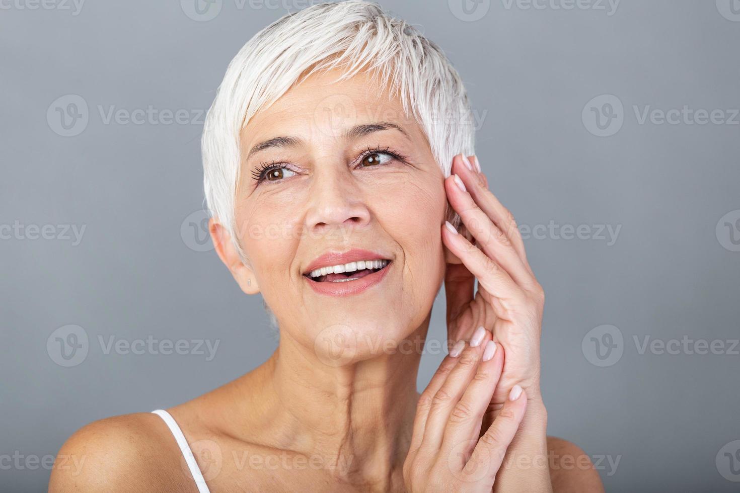 beauté portrait de mature femme souriant avec main sur affronter. fermer visage de content Sénior femme sentiment Frais après anti-âge traitement. souriant beauté à la recherche à caméra avec parfait peau. photo