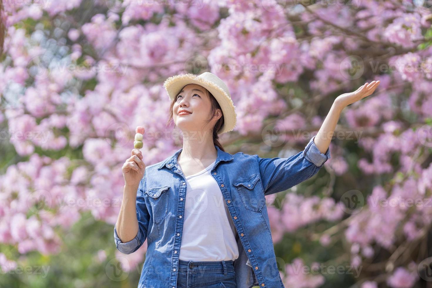 asiatique femme en portant le sucré hanami dango dessert tandis que en marchant dans le parc à Cerise fleur arbre pendant printemps Sakura Festival avec copie espace photo