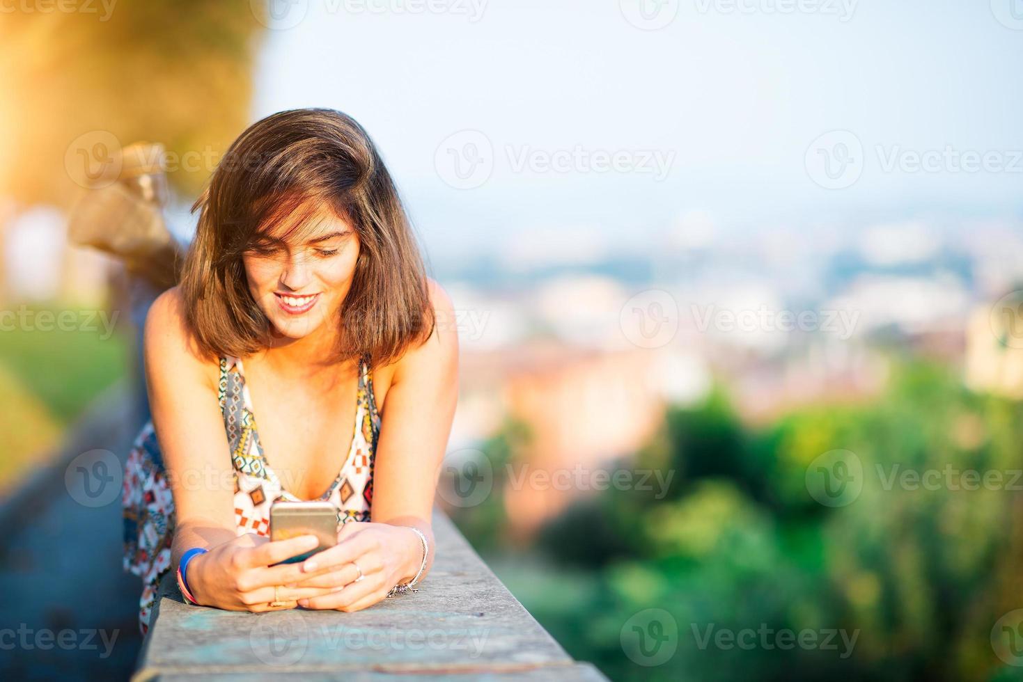 Belle jeune fille sur un mur dans une ville à l'aide de son smartphone photo