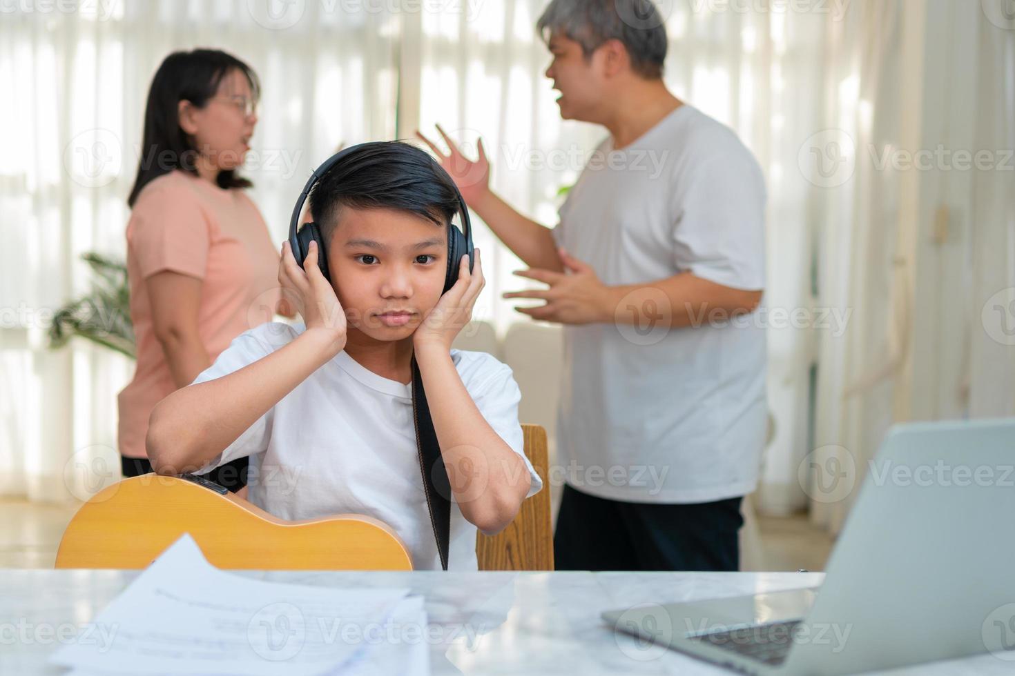 enfant garçon asiatique portant des écouteurs et jouer de la musique forte. afin de ne pas entendre de querelle pendant que les parents se disputent ou se querellent à la maison. problème malheureux dans la famille, problèmes domestiques dans la famille. photo