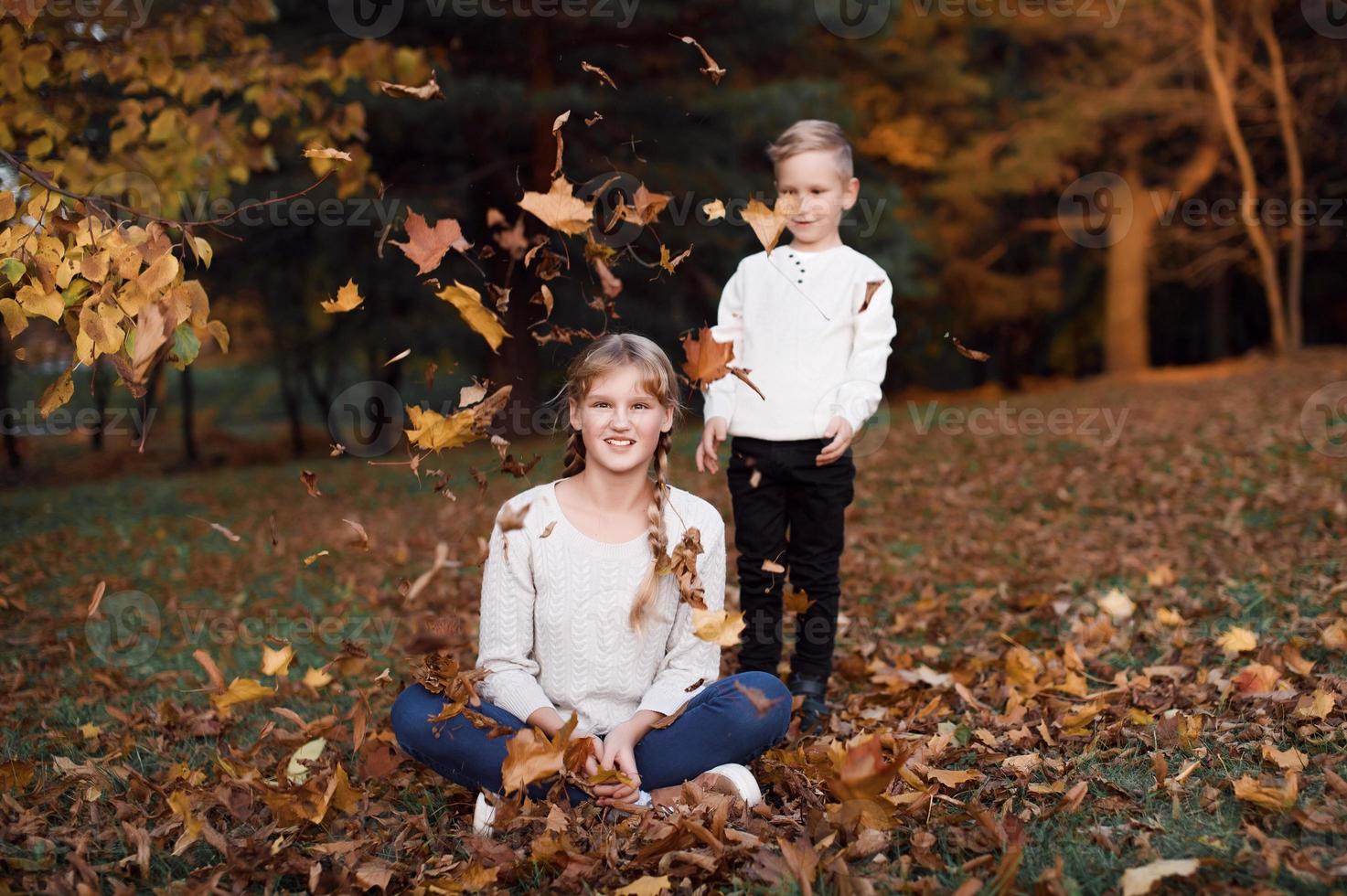content fille et garçon lancer Jaune l'automne feuilles dans le forêt photo