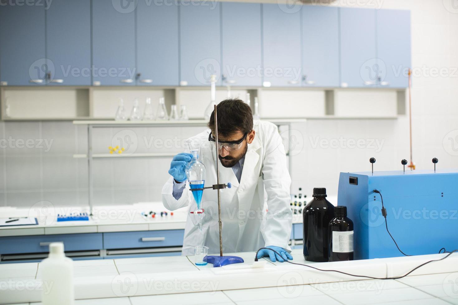 Jeune chercheur travaillant avec un liquide bleu à l'entonnoir de séparation dans le laboratoire photo