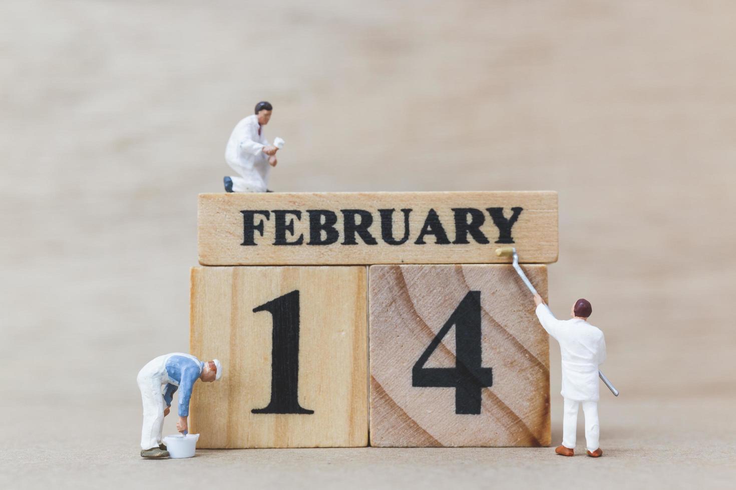 Les gens miniatures peignant des blocs de bois avec le 14 février sur un fond de bois, happy valentine's day concept photo