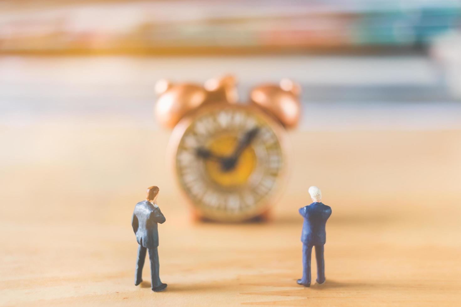 Hommes d'affaires miniatures debout avec une vieille horloge sur un fond de bois photo