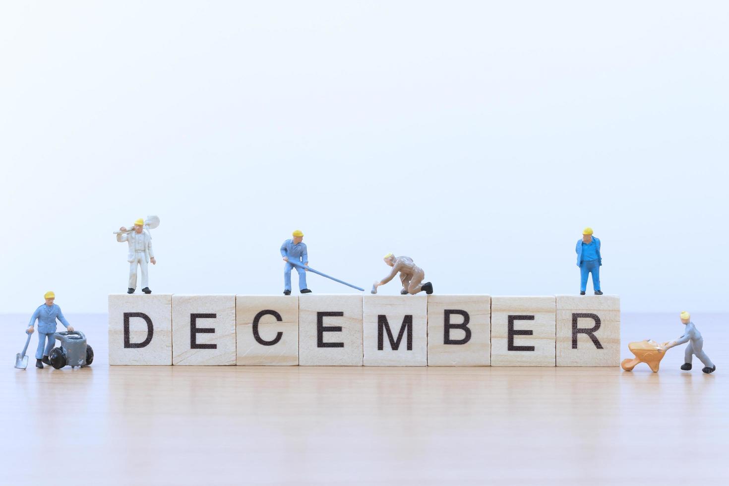 Personnes miniatures travaillant sur des blocs de bois avec le mot décembre sur un plancher en bois photo