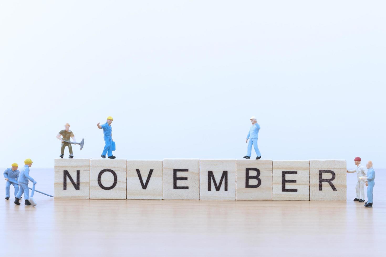 Personnes miniatures travaillant sur des blocs de bois avec le mot novembre sur un plancher en bois photo