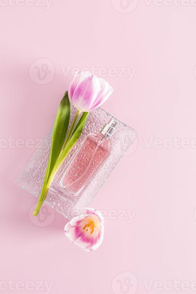 une bouteille de délicat aux femmes parfum ou vaporisateur mensonges sur une verre le soulagement plateau avec une tulipe. verticale voir. rose Contexte. arôme présentation. photo