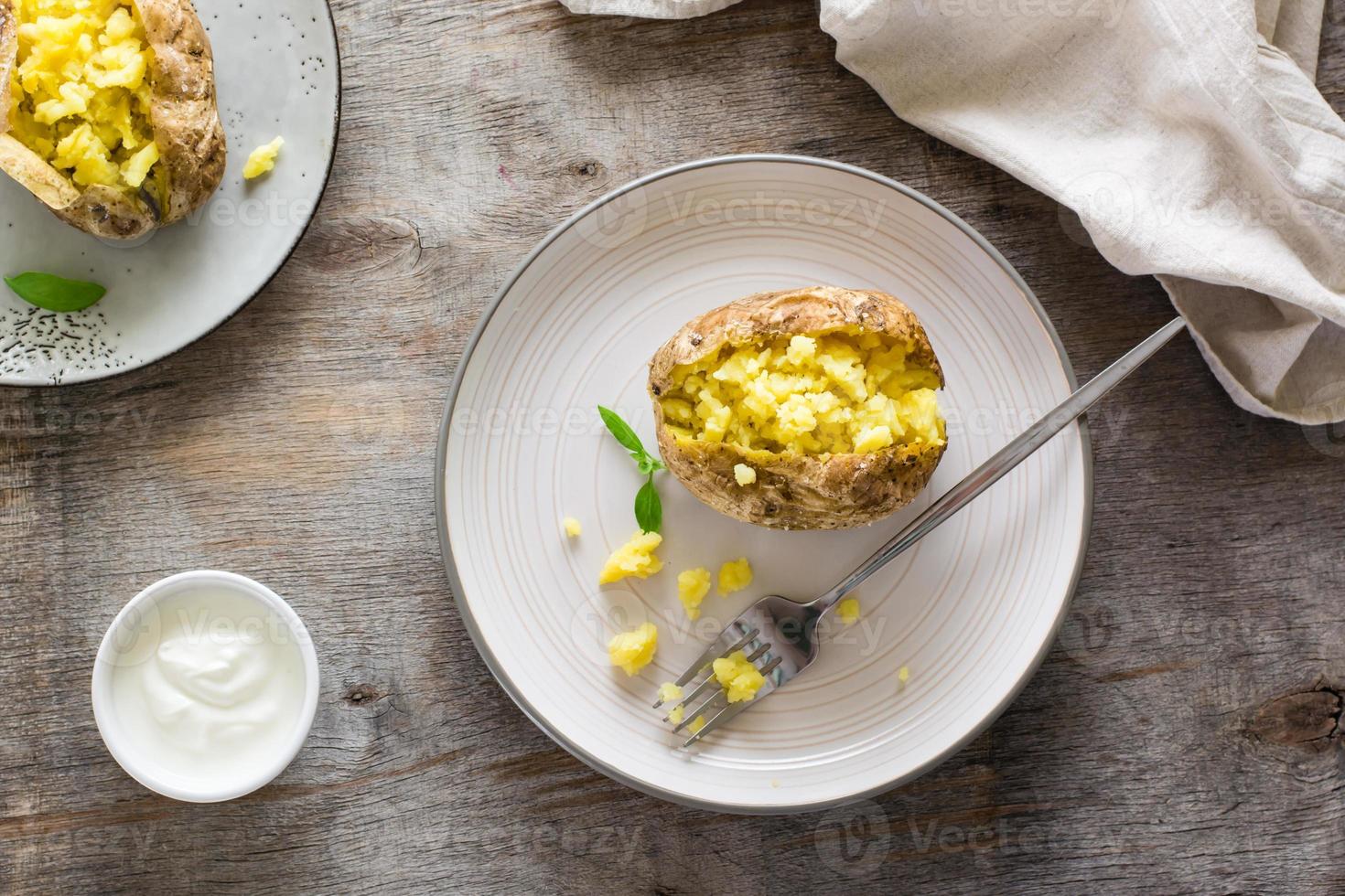 cuit patates dans leur peaux sur assiettes et une bol de acide crème sur une en bois tableau. végétarien Naturel aliments. Haut vue photo