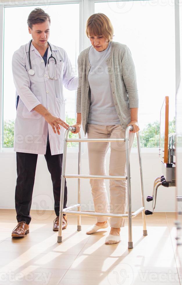 caucasien Masculin médecin portion femelle patient essayer à marcher avec marcheur. médecin est examiner le patient dans le hôpital. photo